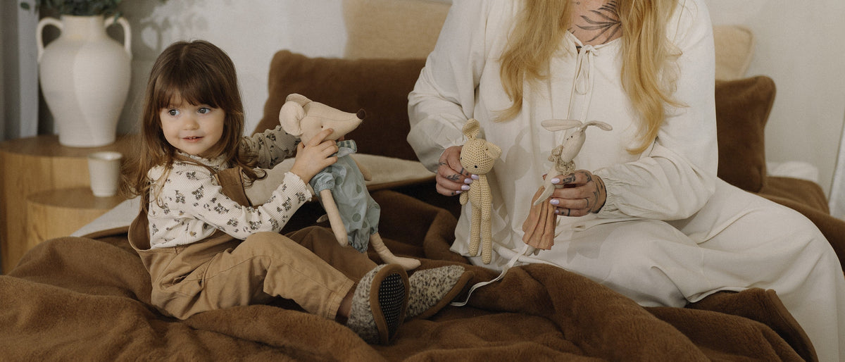 Un tout-petit et un adulte jouent sur un lit avec une couverture en laine marron