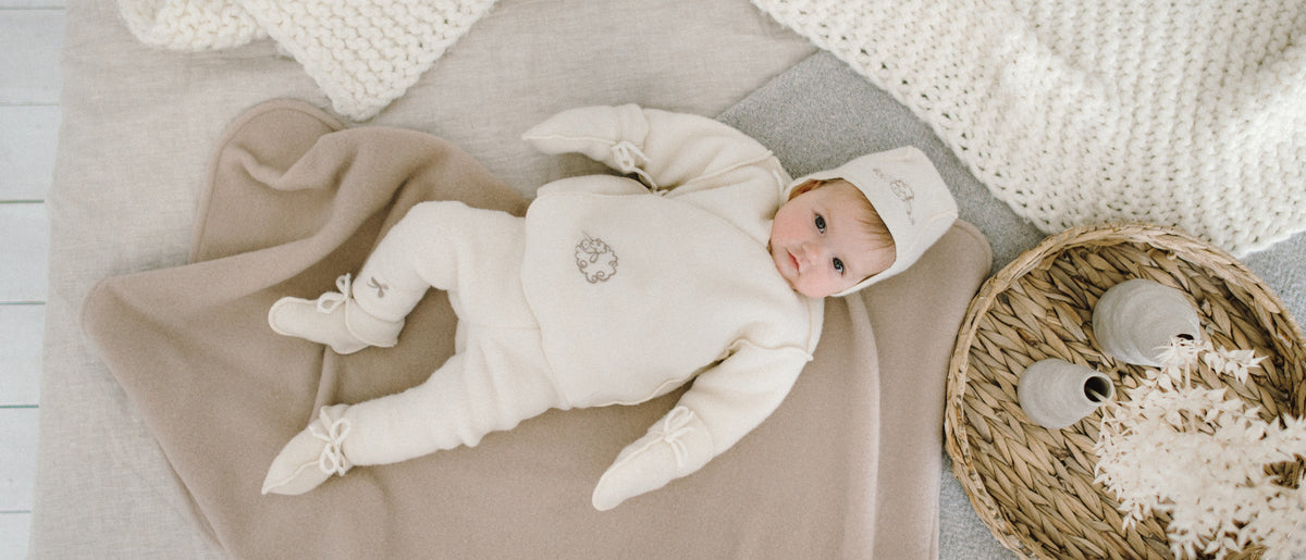 Bébé en combinaison, bonnet et chaussons en mérinos sur une couverture douce