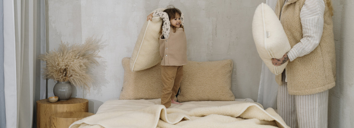 Enfant jouant sur un lit avec des coussins en laine et un plaid en laine mérinos